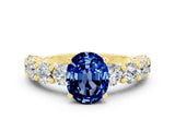 Yellow gold Oval Cut Blue Sapphire Prong Setting with Side Stones on a Pave Band