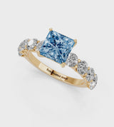 Yellow gold Fancy Blue Princess Cut Diamond Prong Setting with Side Stones on a Pave Band
