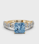Yellow gold Fancy Blue Princess Cut Diamond Prong Setting with Side Stones on a Pave Band