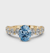 Yellow gold Fancy Blue Oval Cut Diamond Prong Setting with Side Stones on a Pave Band